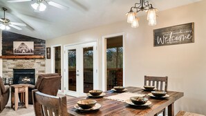 A dining area with a wooden table set for four, surrounded by chairs, with a fireplace and a 'Welcome' sign on the wall. - Deer Browse Hideaway: Sink a Putt, Soak It In (Sevierville)