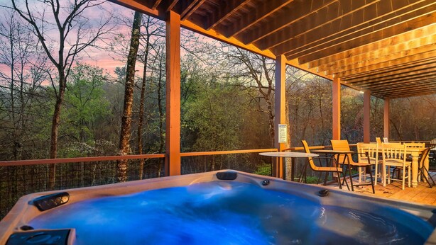 A hot tub with a wooden deck and chairs, surrounded by trees. - Deer Browse Hideaway: Sink a Putt, Soak It In (Sevierville)