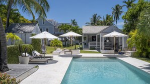 A pool area with lounge chairs and umbrellas, surrounded by palm trees and a house. - Luxury Holiday Estate with Pool, minutes walk from Pink Sands beach (Harbour Island)