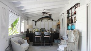 A room with a ceiling fan, a bar area with stools, and a bookshelf with various items. - Luxury Holiday Estate with Pool, minutes walk from Pink Sands beach (Harbour Island)