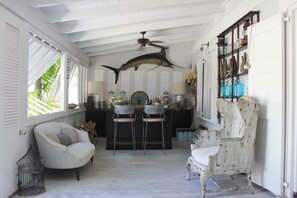 Quarto com ventoinha no teto, área de bar com banquetas e estante com diversos objetos.