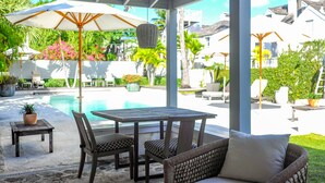 An outdoor patio with a pool, a table, chairs, and a large umbrella. - Luxury Holiday Estate with Pool, minutes walk from Pink Sands beach (Harbour Island)