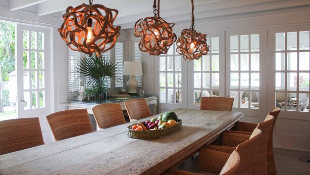 A dining area with a long wooden table, wicker chairs, and hanging pendant lights. - Luxury Holiday Estate with Pool, minutes walk from Pink Sands beach (Harbour Island)