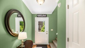 A hallway with a wooden bench, a round mirror, a door labeled "AIRPLANE HANGAR," and a staircase. - Piper's Landing: Touch Down in the Smokies (Gatlinburg)