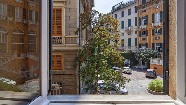 Blick aus einem Fenster auf eine Straße mit parkenden Autos und Gebäuden mit Balkonen.