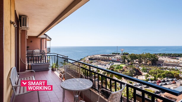 Un balcon avec une table et des chaises, donnant sur une ville côtière et la mer.
