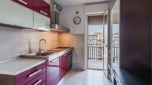 Une cuisine compacte équipée d’une cuisinière à gaz, d’un évier et de meubles de rangement modernes. Une horloge est visible au mur, et la cuisine donne sur un balcon avec vue sur la ville.