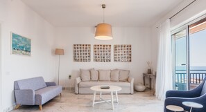 A modern living room with a sofa, a coffee table, and a blue armchair. There is a painting on the wall and a lamp. - Piazza Europa Landscape by Wonderful Italy (Catania)