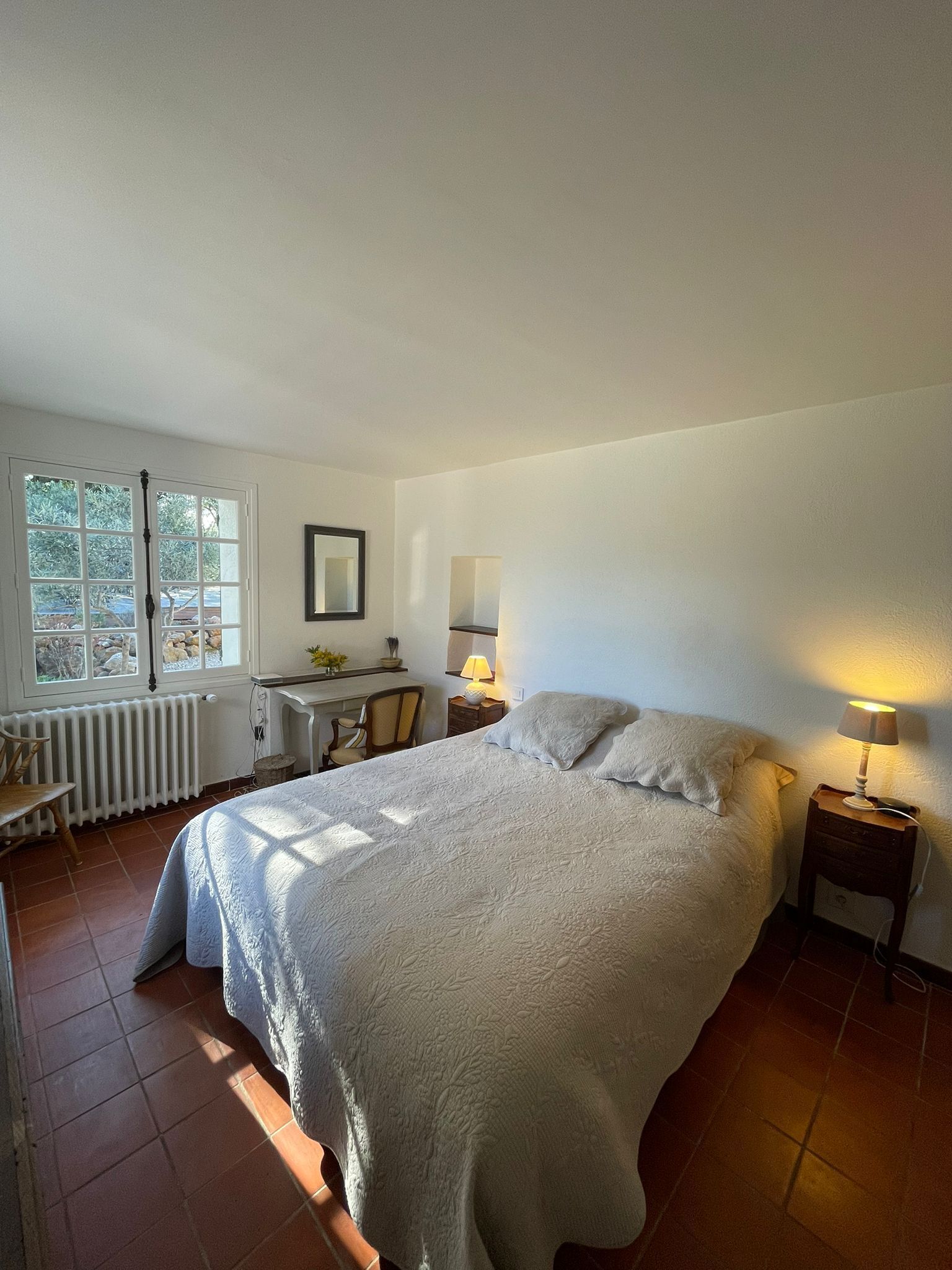A bedroom with a large bed, a desk, a chair, a lamp, and a radiator.