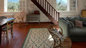 Un vaste salon agrémenté d’un escalier en bois, d’un coin repas et offrant une vue sur l’extérieur grâce à de grandes fenêtres.