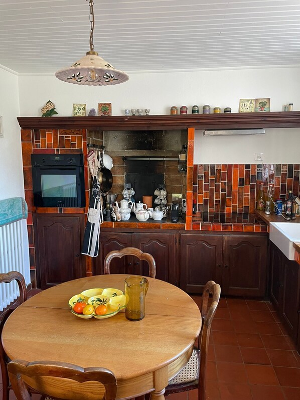 A kitchen with a dining table, chairs, a hanging light fixture, a built-in oven, and a tiled backsplash. - Charming Provençal villa with a pool surrounded by olive groves (Aups)
