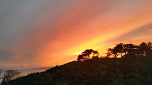 A sunset over a hilly landscape with trees and a body of water in the distance.