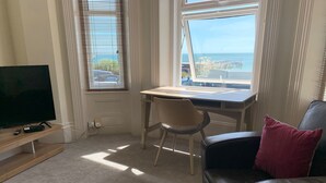 A living room with a TV, a desk, a chair, and a leather couch with a red pillow. - Beach Front 2-bed Apartment With Deck & BBQ (Bournemouth)