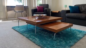 A modern living room with a wooden coffee table, a blue shag rug, a black leather sofa, and a chair. - Beach Front 2-bed Apartment With Deck & BBQ (Bournemouth)