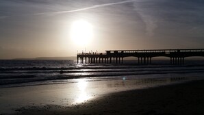A pier extending into the ocean with the sun setting in the background. - Beach Front 2-bed Apartment With Deck & BBQ (Bournemouth)