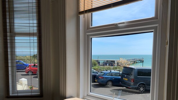 A room with a large window overlooking a parking area and a pier. - Beach Front 2-bed Apartment With Deck & BBQ (Bournemouth)