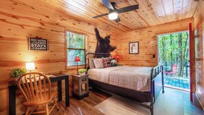 L'intérieur d'une cabane comprend un lit, un bureau, une chaise, un ventilateur de plafond et une fenêtre donnant sur la forêt.