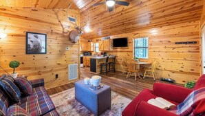Un intérieur de chalet chaleureux comprenant un salon, une cuisine et un coin repas, avec des murs en bois et un ventilateur de plafond.