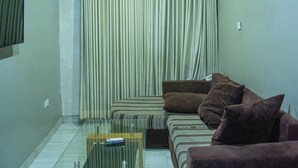 A living room with a glass coffee table, a sofa, and a television on the wall. - Kelin Hotel & Suite (Lagos)