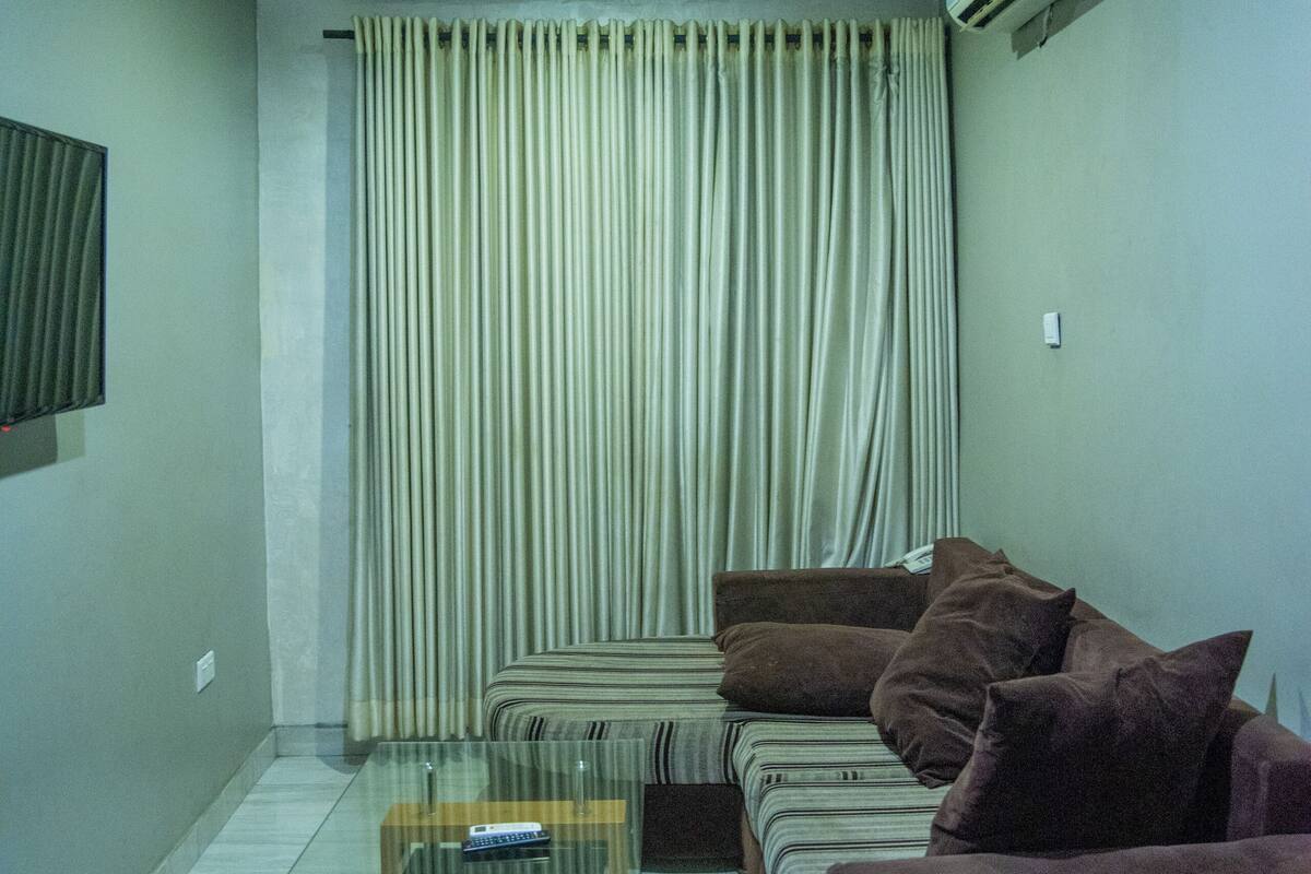 A living room with a glass coffee table, a sofa, and a television on the wall.