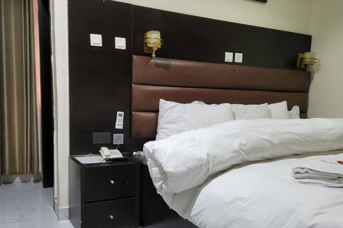 A hotel room with a bed, a nightstand with a phone, and a painting on the wall.