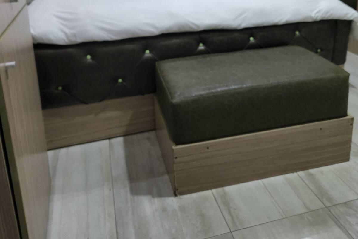 A bedroom with a large bed, a wooden headboard, a bedside table, and a small bench.