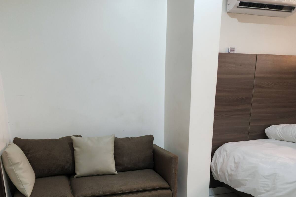 A modern room with a brown sofa, a white bed, and a white tiled floor.