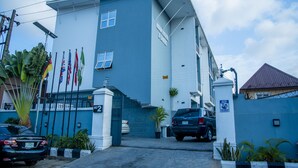 A hotel with a blue exterior, multiple flags, and a gated entrance. - Kelin Hotel & Suite (Lagos)
