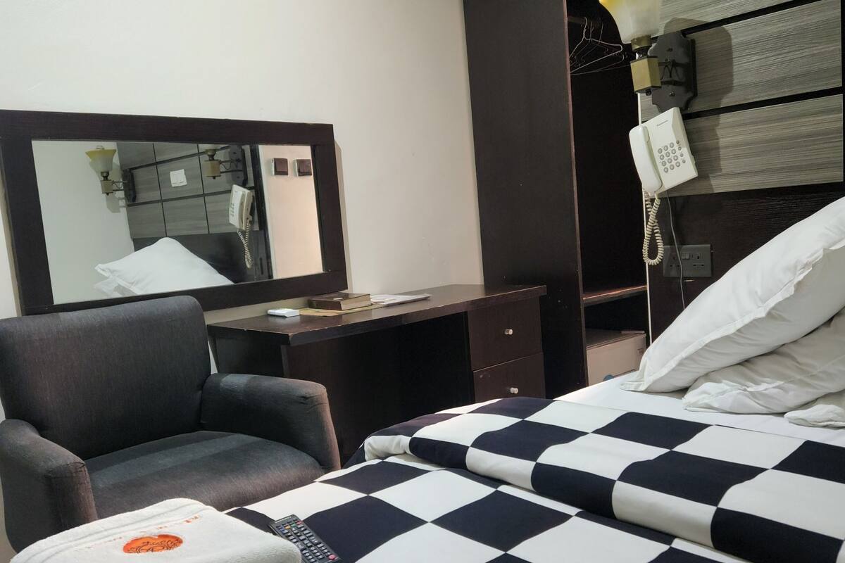 A hotel room with a bed, a desk, a chair, a telephone, and an air conditioning unit.