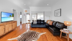 A modern living room with a television, leather sofa, wooden flooring, and a zebra-patterned rug. - Quay Haven – complete relaxation & fun (Callala Beach)