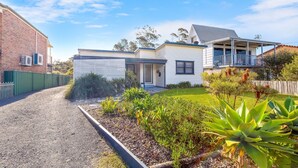 A two-story house with a front porch, a garage, and a well-maintained garden with various plants. - Quay Haven – complete relaxation & fun (Callala Beach)