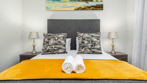 A neatly made bed with a yellow bedspread, two pillows with a camouflage pattern, and a pair of white towels folded on top. - The Axis 212 (Cape Town)