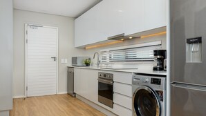 A modern kitchen with white cabinets, a built-in oven, a washing machine, and a coffee maker. - The Axis 212 (Cape Town)