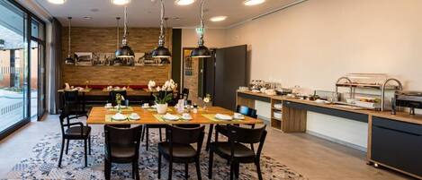 Un comedor moderno con una mesa de madera dispuesta para cuatro personas, rodeada de sillas negras. Hay lámparas colgantes sobre la mesa y una alfombra estampada en el suelo.