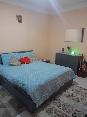 A bedroom with a bed, pillows, a bedside table, a lamp, and a mirror.
