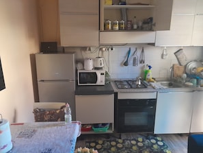 Eine kompakte Küche mit Kühlschrank, Mikrowelle, Gasherd und Spüle. Über der Arbeitsfläche befinden sich Schränke und ein kleiner Tisch mit Tischdecke.
