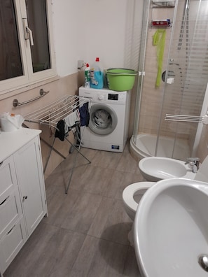 A modern bathroom with a washing machine, a shower, and a toilet.