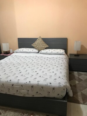 Ein ordentlich bezogenes Bett mit einer gemusterten Tagesdecke, einem Zierkissen und zwei Nachttischlampen auf einem Nachttisch.