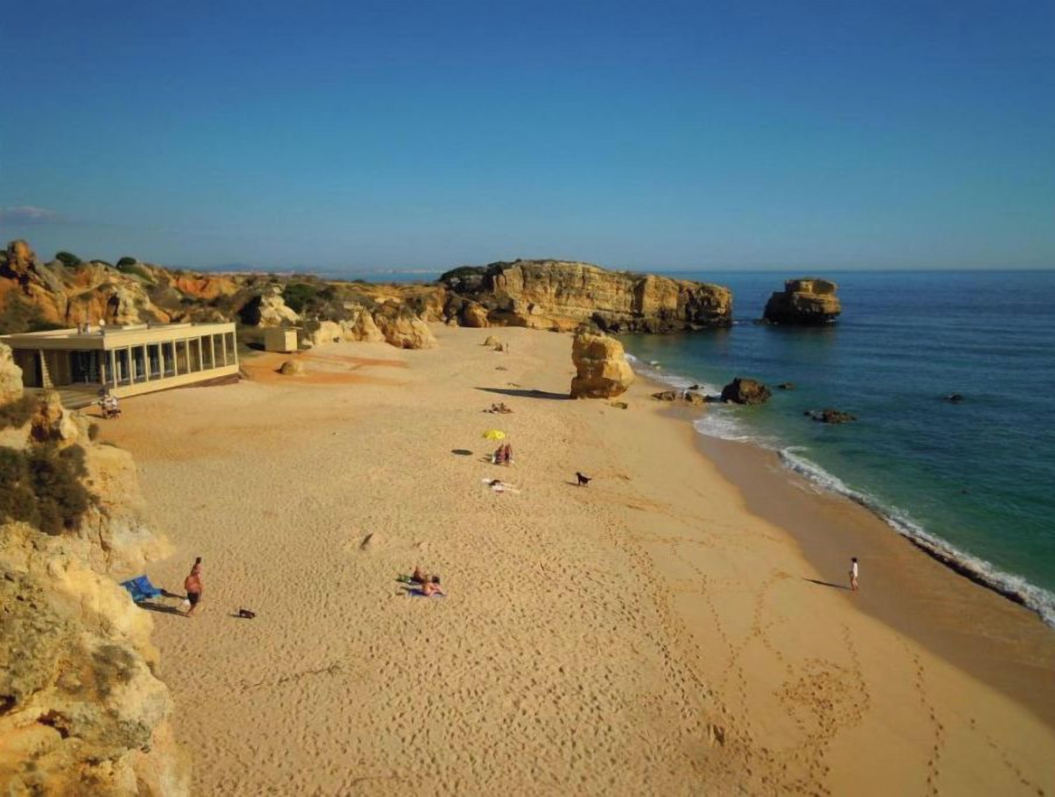 Une plage avec un ciel dégagé, des falaises rocheuses et quelques personnes.