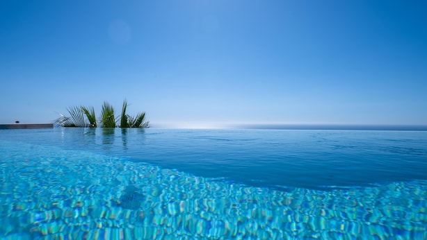 Ein klares, blaues Schwimmbecken mit Blick auf den Ozean und Palmen im Hintergrund.