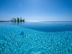 Una piscina azul cristalina con vistas al océano y palmeras al fondo.