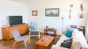 En stue med fjernsyn, træskab, grå og hvide sofaer, et sofabord og en reol.