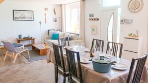 Et spiseområde med et bord dækket til fire personer, en sofa og et vindue med gardiner.