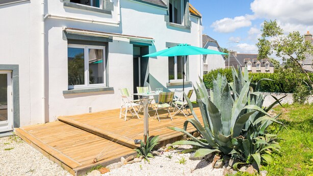 Et toetagers hus med træterrasse, udendørs møbler og en stor aloe plante.