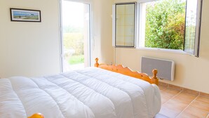 Un dormitorio con cama, ventana con vista a vegetación, radiador y puerta.