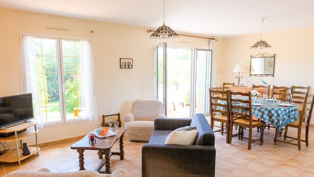 Una sala de estar con un sofá, sillones, televisor y una mesa de comedor con sillas.