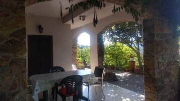 Eine Terrasse im Freien mit Tisch und Stühlen, Steinmauern und Blick ins Grüne.