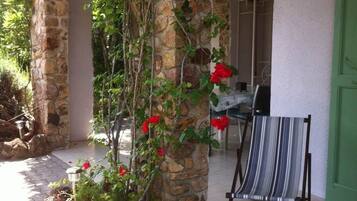 Un pilar de piedra con plantas trepadoras y flores rojas, una silla de playa a rayas y una puerta verde.