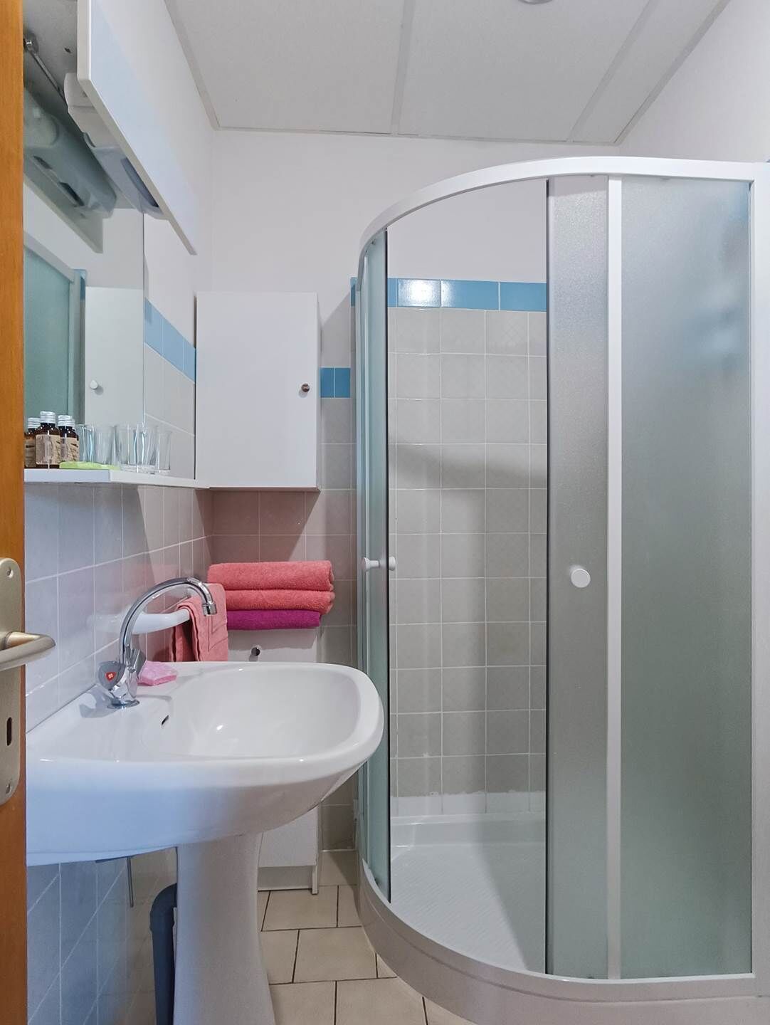 A bathroom with a white sink, a glass shower enclosure, and a cabinet with toiletries.