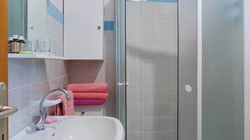 A bathroom with a white sink, a glass shower enclosure, and a cabinet with toiletries.